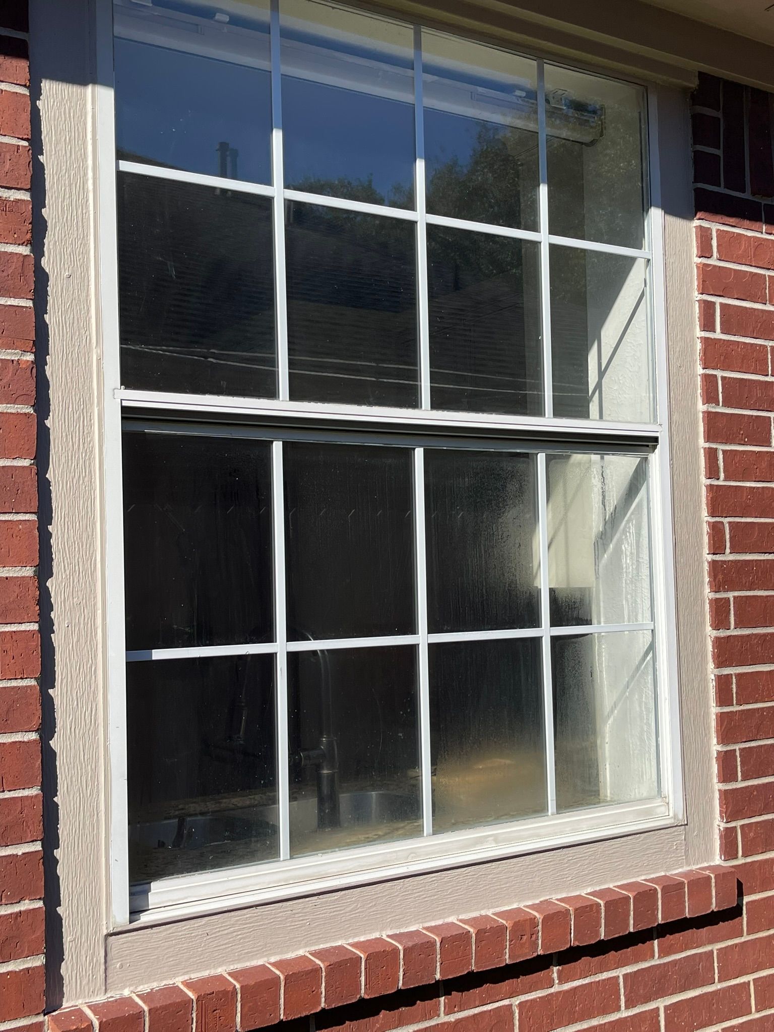 A double-hung white window with a grid pattern, set into a red brick exterior wall with a light-colored frame.
