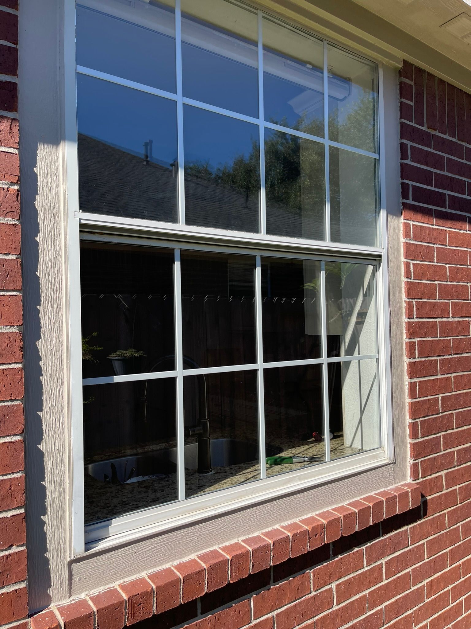 A white single-hung window with a grid pattern, installed in a red brick exterior wall.