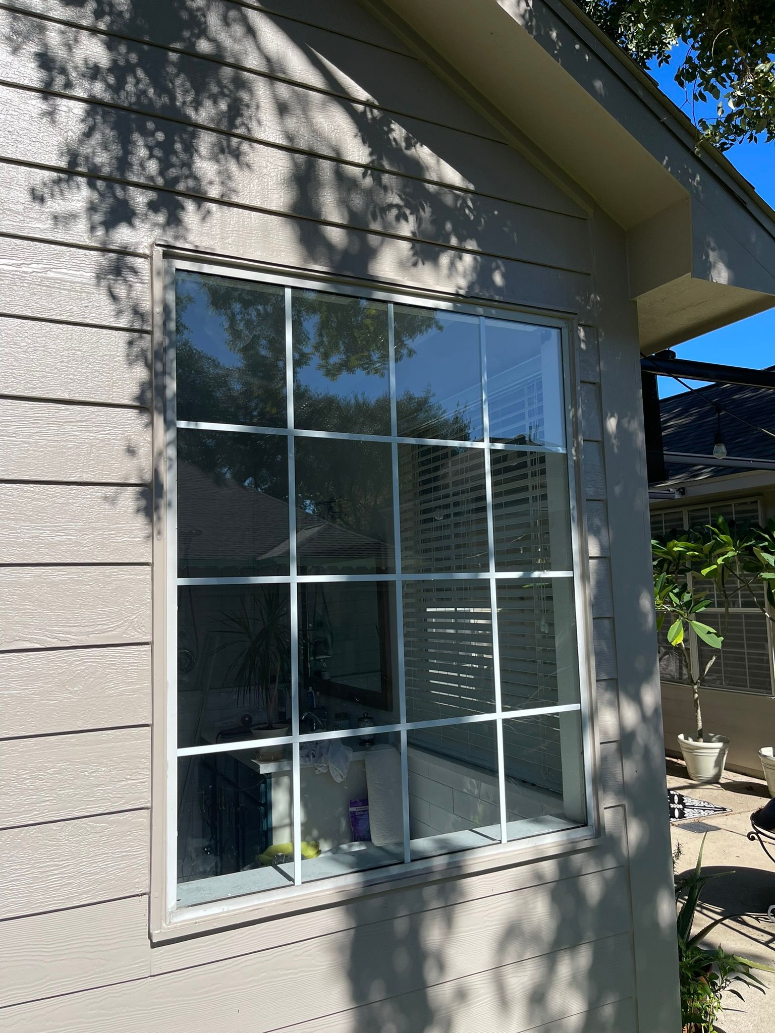 A large, multi-pane window with white frames set into the exterior wall of a house with beige horizontal siding.