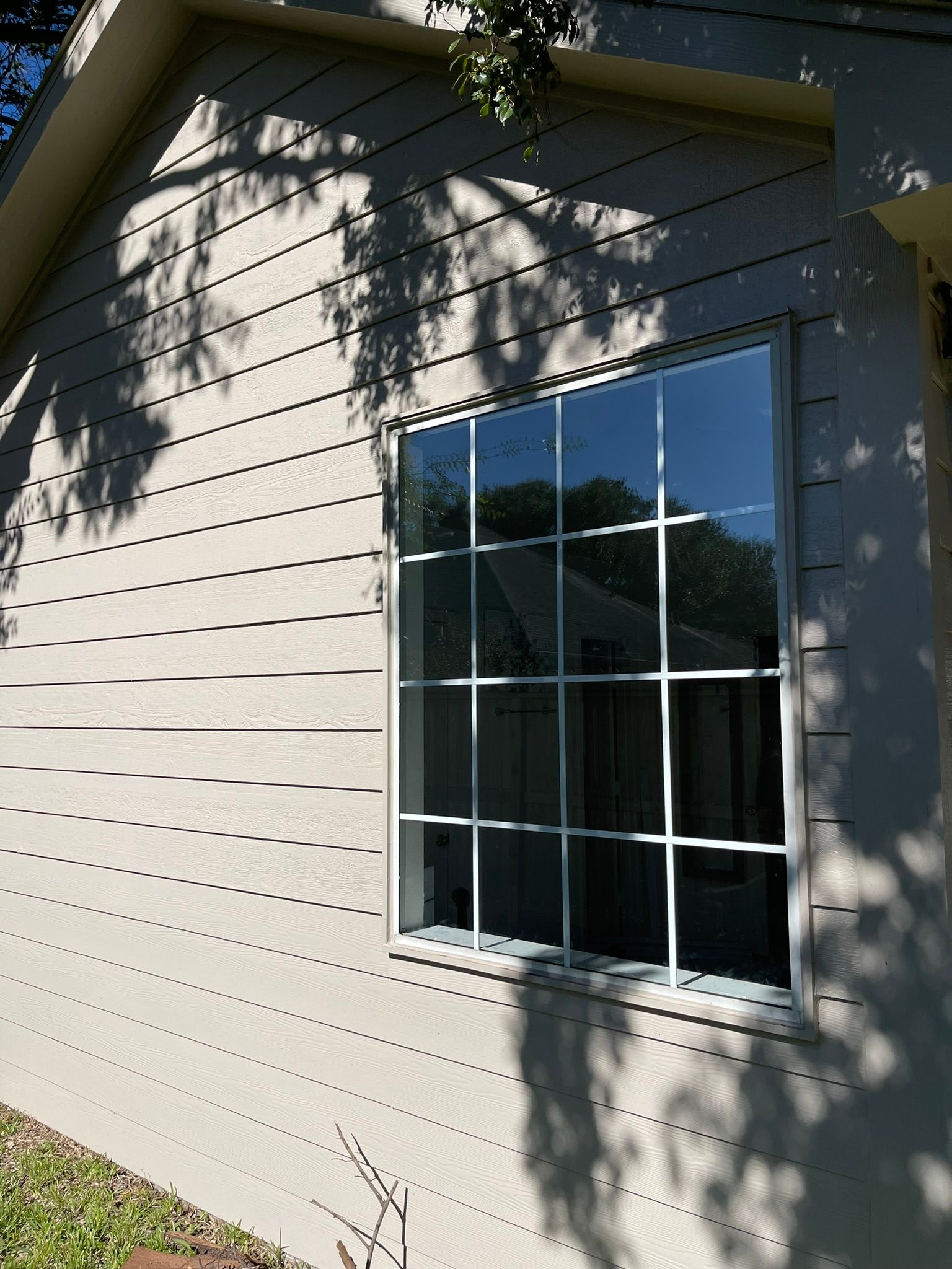 A window with a white grid frame on the light gray, horizontal-sided exterior wall of a house.