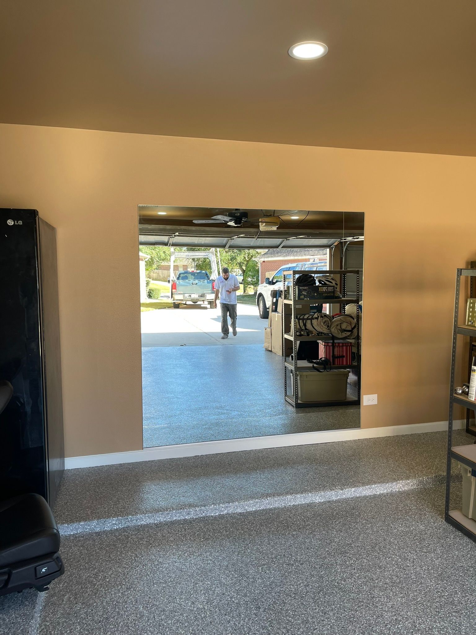 A view from inside a garage looking out through a large wall opening toward a person standing on the driveway.