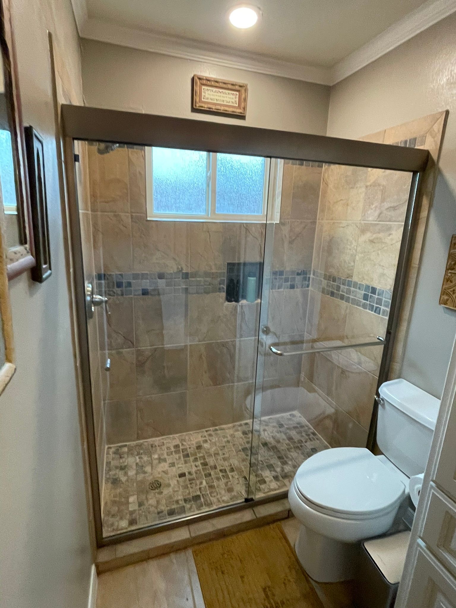 A bathroom features a walk-in shower with stone tile walls, a pebbled floor, a glass door, and an adjacent white toilet.