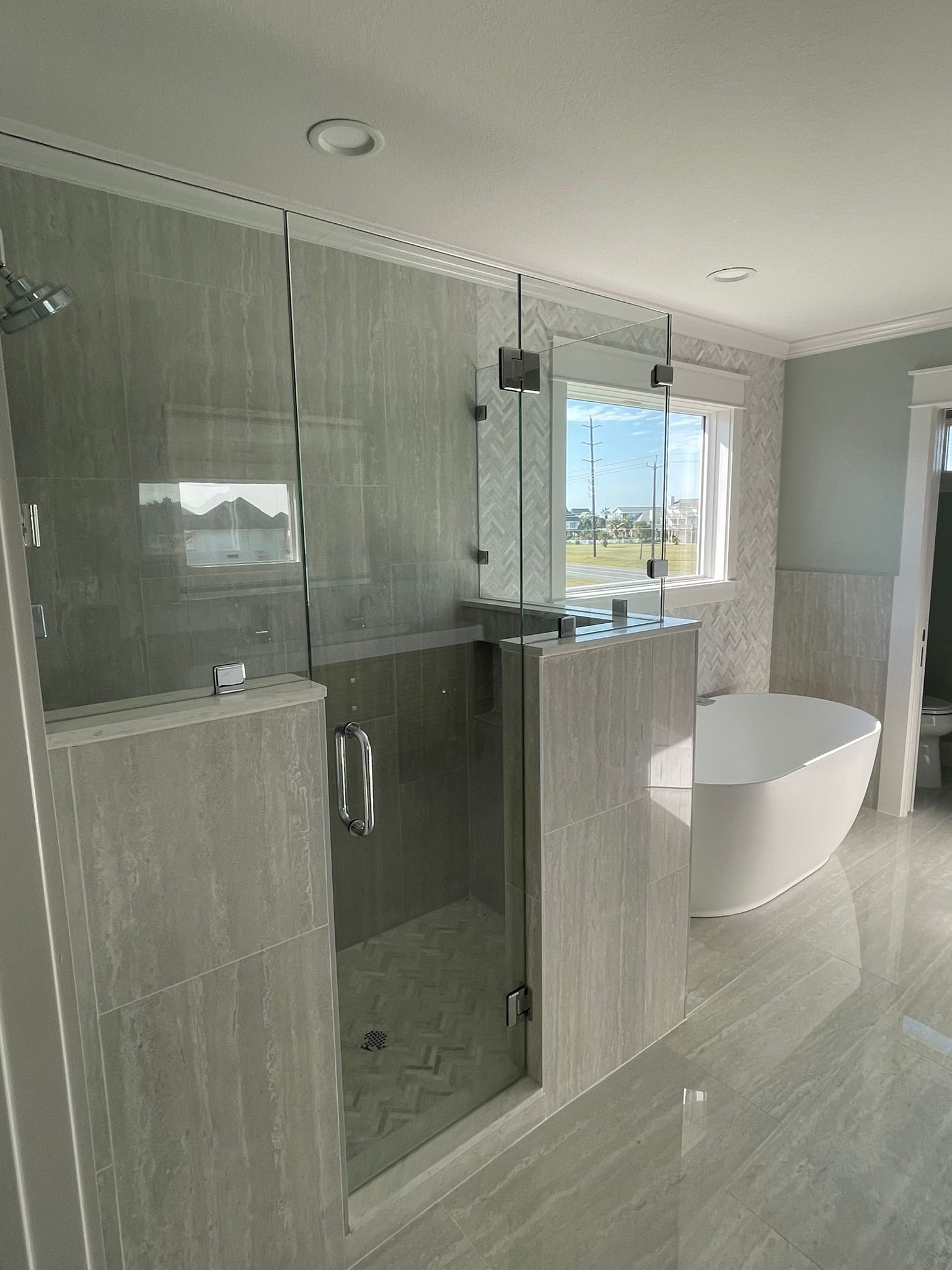A modern bathroom featuring a glass-enclosed shower with grey stone tiles next to a freestanding white bathtub.