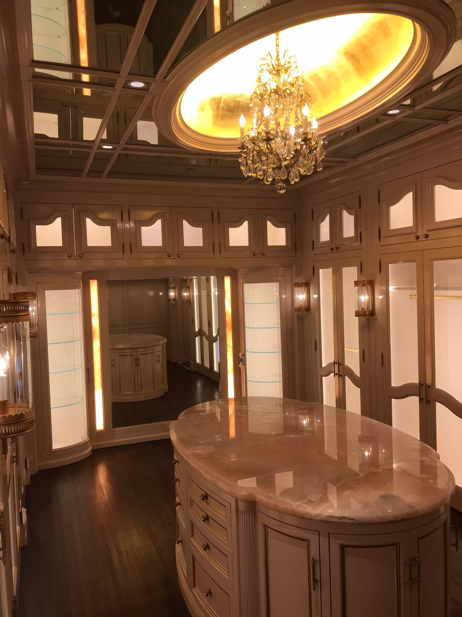 A luxurious walk-in closet with cream-colored cabinetry, a central marble-topped island, and a crystal chandelier.