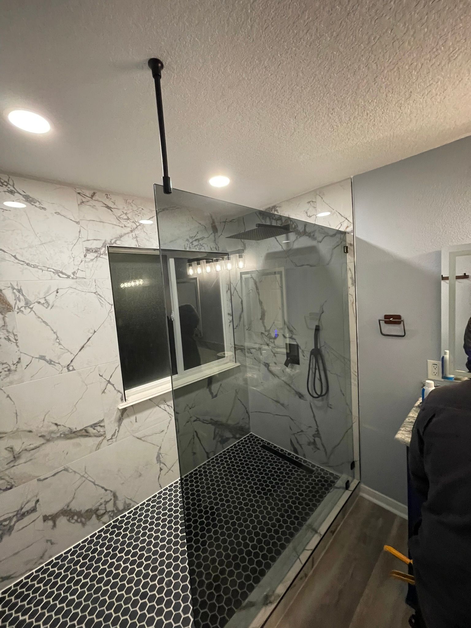 A glass shower enclosure with white marble-patterned walls and a black patterned tiled floor in a modern bathroom.