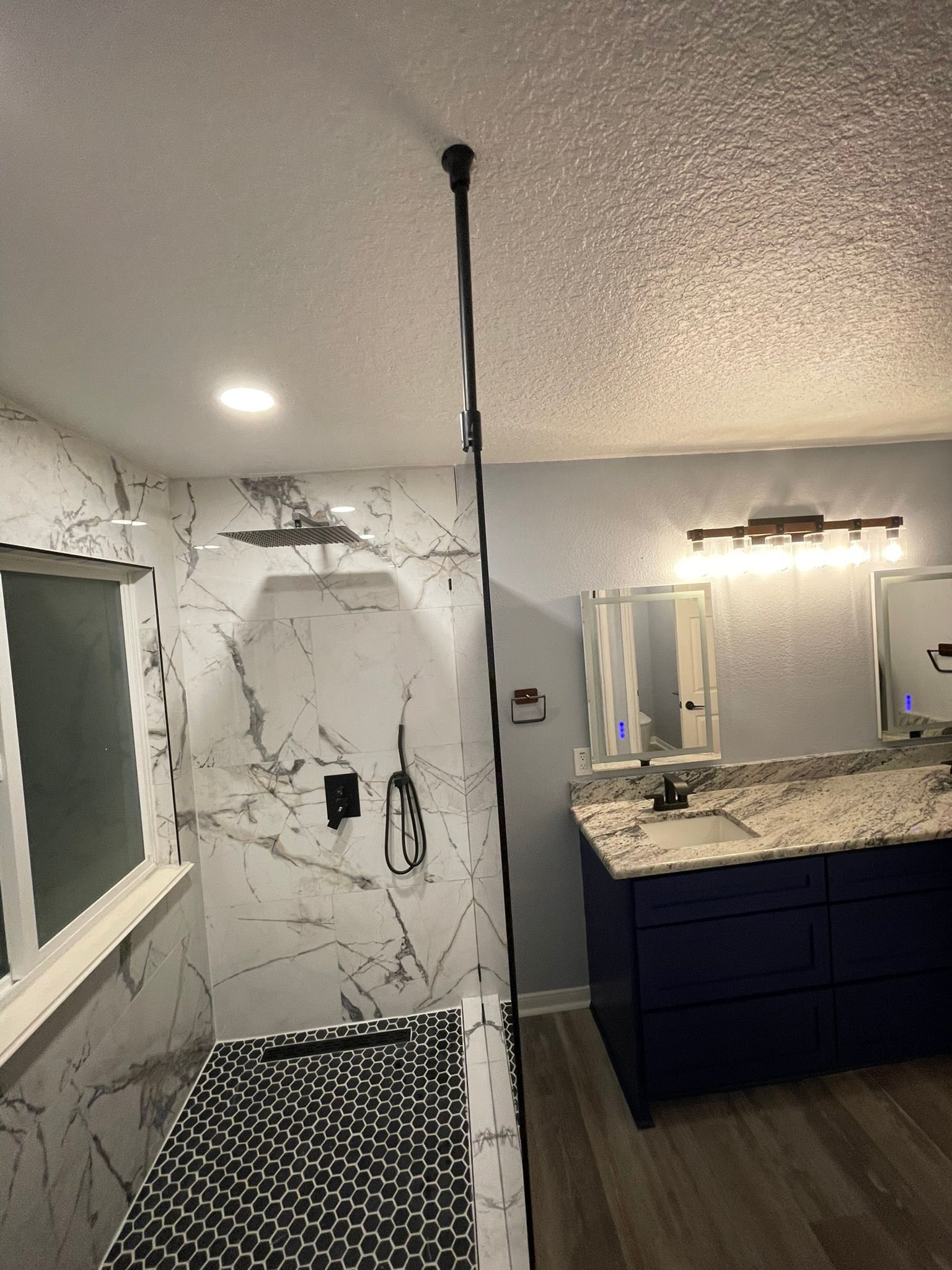 A bathroom with a dark blue vanity, marble-patterned shower walls, and a black cord hanging from the ceiling.