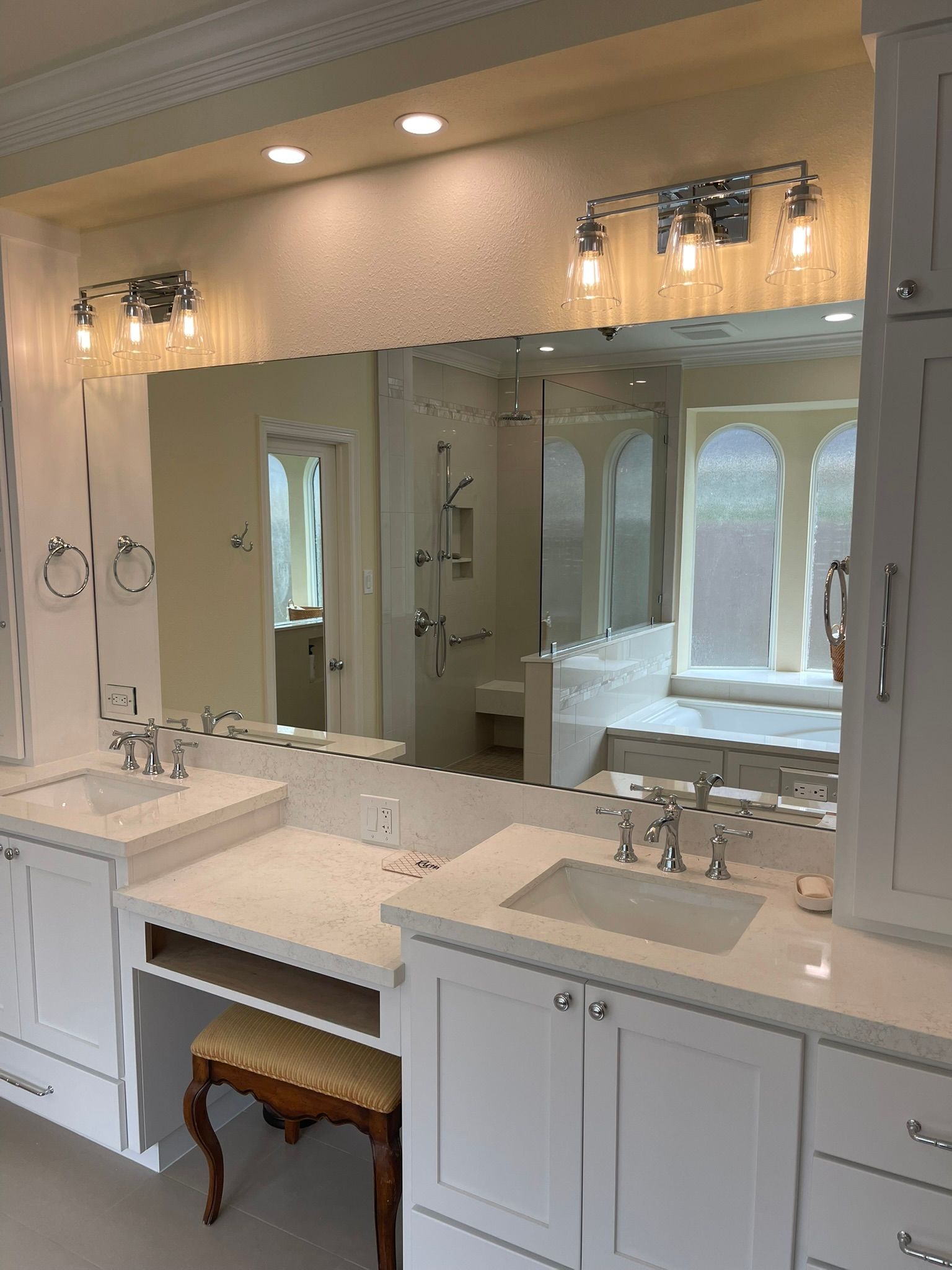 A white double vanity with a central makeup station, quartz countertops, chrome fixtures, and sconce lighting.