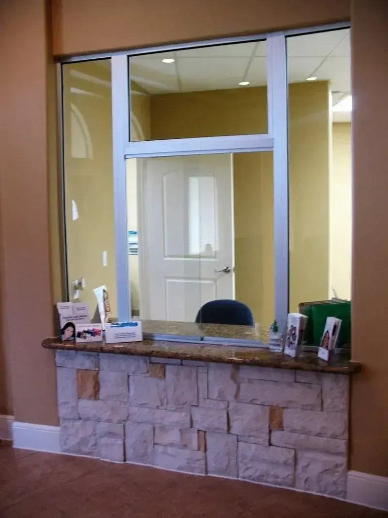 A reception desk with a stone base and a glass transaction window, viewed from a waiting area.