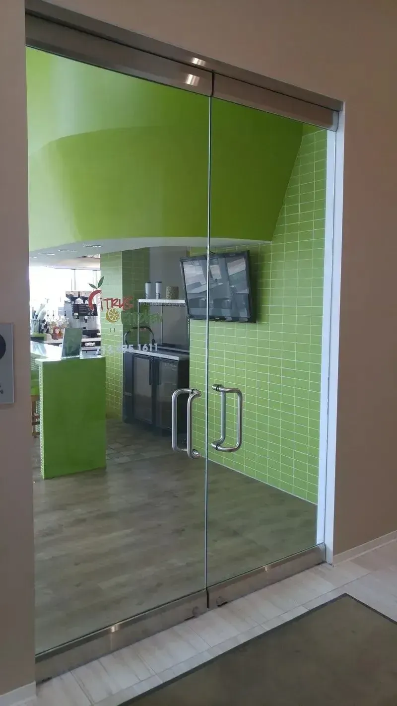 Double glass doors with silver handles open into a modern room featuring lime green walls, a kitchen counter, and a TV.