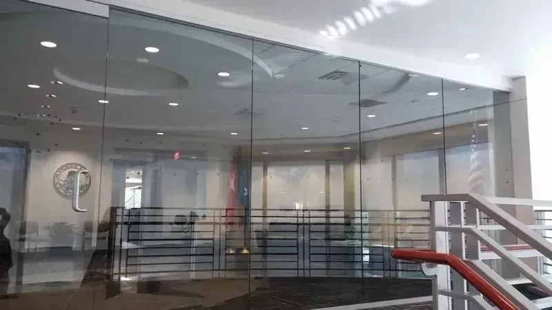 A glass-walled office area with a logo on the left, viewed from behind a white stair railing with a red handrail.
