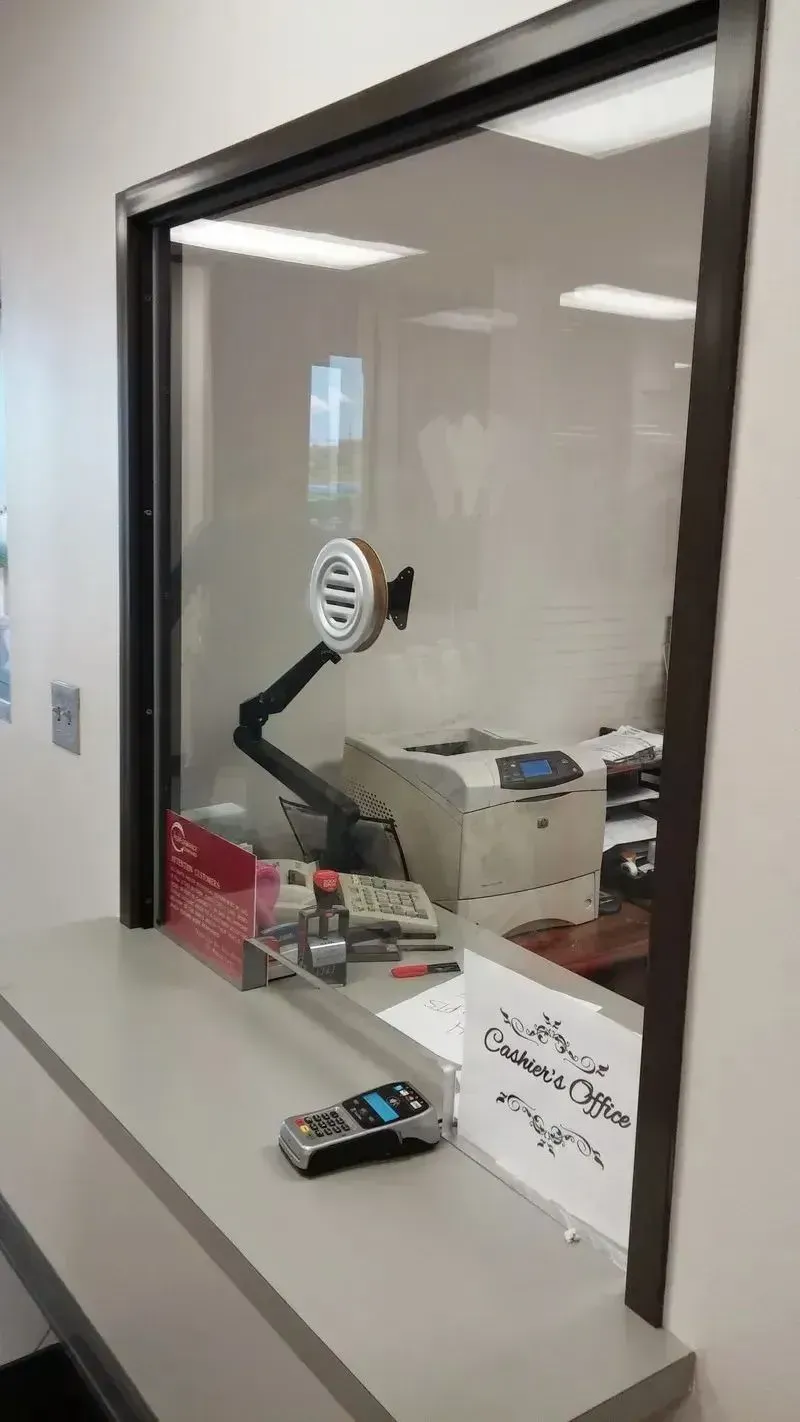 A service window with a payment terminal and a small circular intercom mounted on the glass partition.