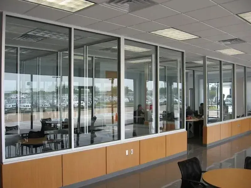 Modern office interior featuring glass-walled meeting rooms with wooden panels, chairs, and tables on a polished floor.