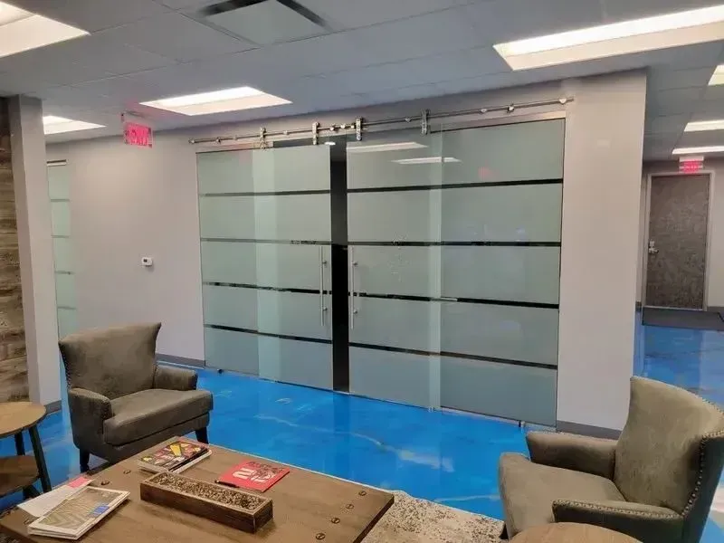 A modern office waiting area features two gray armchairs facing a wooden coffee table in front of frosted sliding doors.