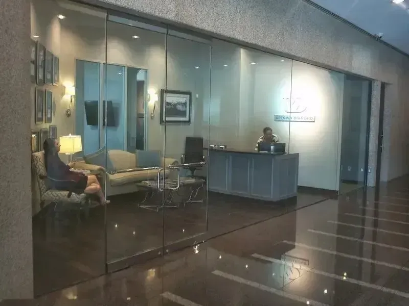 A reception office with a glass front, containing a person seated at a desk and another person on a sofa.