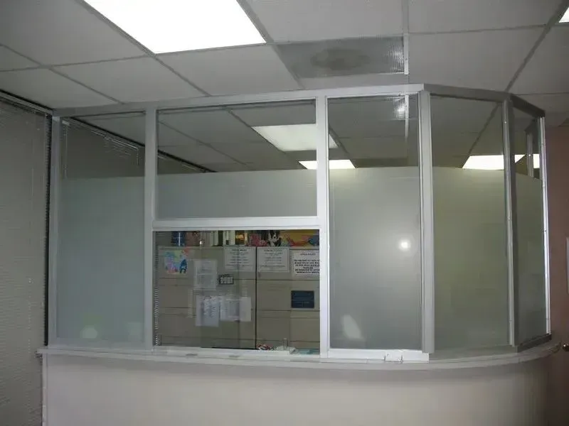 A reception desk with a silver-framed glass partition featuring frosted privacy panels and a clear service window.