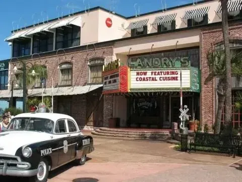 A vintage black and white police car parked in front of a Landry’s restaurant with a 