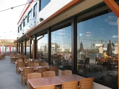 Outdoor restaurant patio with wood-colored chairs and tables aligned along a building with large glass windows.