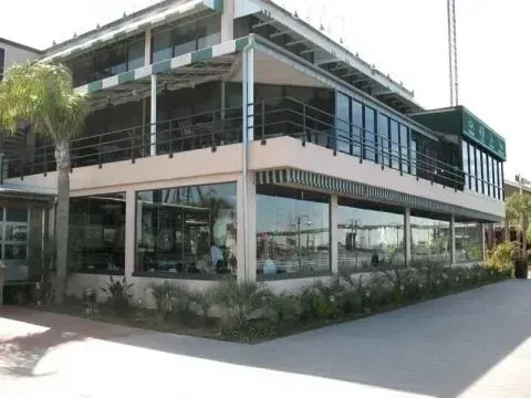 A multi-story commercial building with floor-to-ceiling windows, outdoor seating on the upper deck, and palm trees.