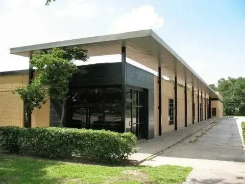 A long, single-story modern commercial building with a large overhanging metal roof, glass entrance, and tan brick walls.