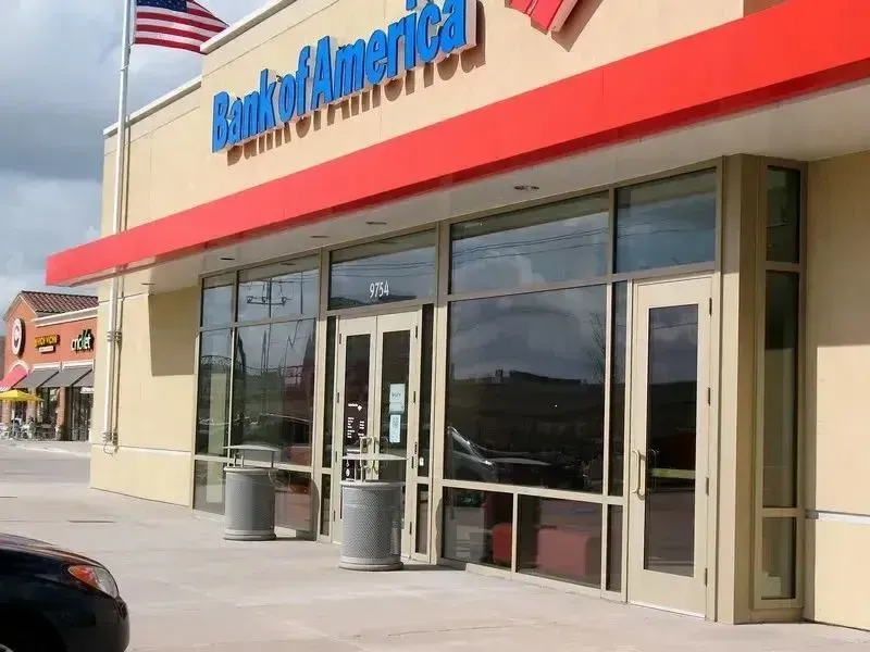 A Bank of America branch exterior with a red awning, glass storefront, and an American flag on a pole.