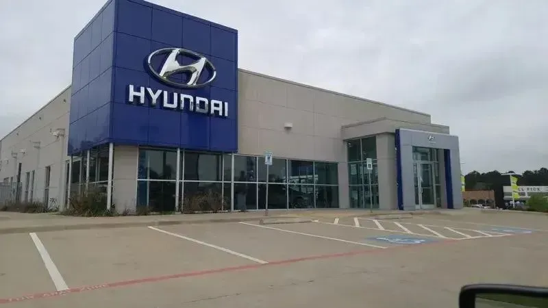 A large Hyundai car dealership building with a prominent blue branding tower and glass windows, seen from a parking lot.