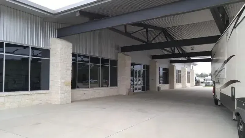 A covered building entrance with stone pillars, glass windows, and a large recreational vehicle parked on the right.