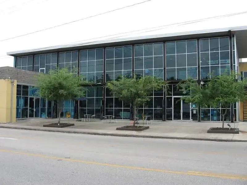 A two-story commercial building with a large glass facade, framed by three small trees on a concrete sidewalk.