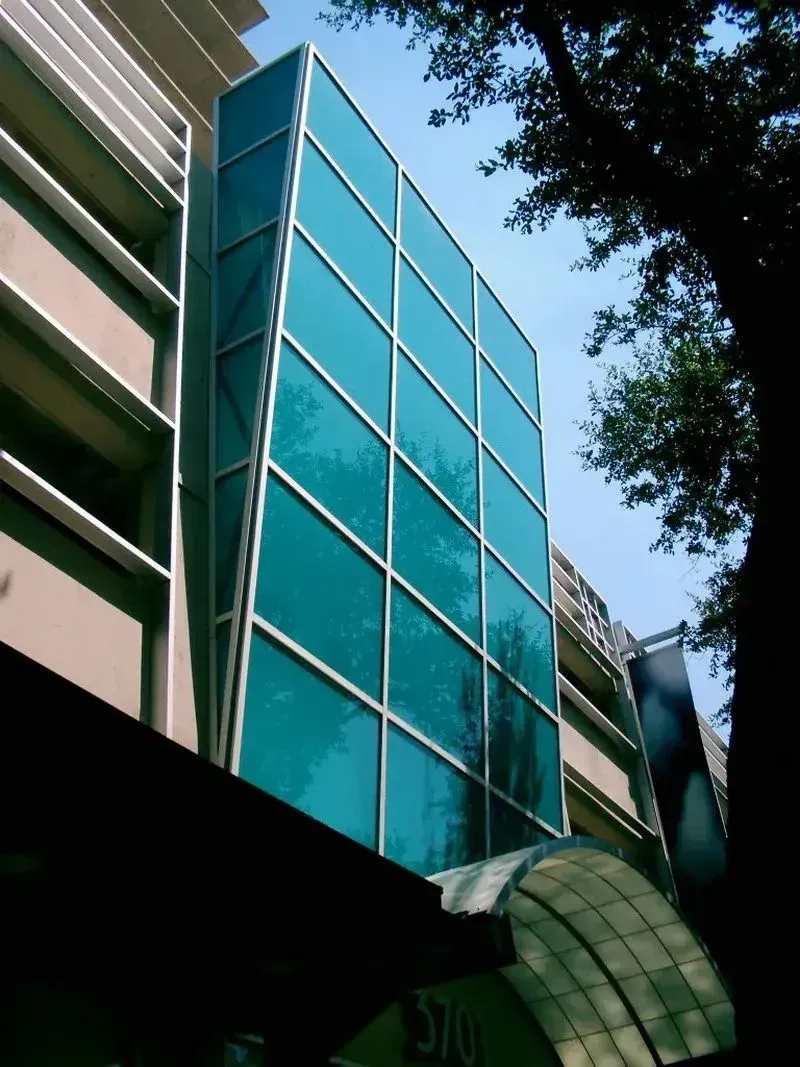 A low-angle view of a modern building facade with a tall, rectangular section of turquoise reflective glass panels.