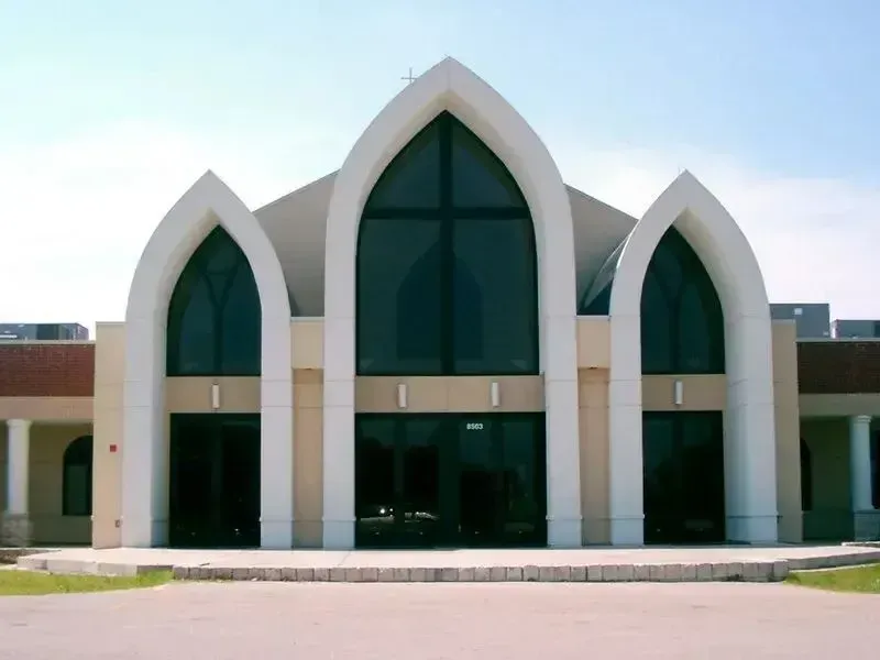 Modern church building facade with three prominent, white-trimmed pointed arches and large glass windows.