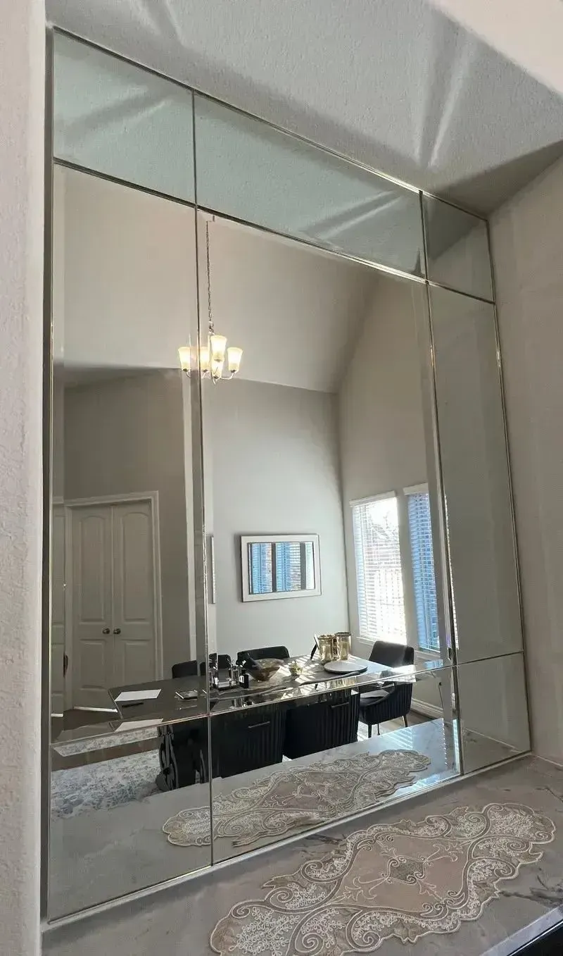 Large wall-mounted mirror panels in a home dining room, reflecting a dining table, chairs, and a chandelier.