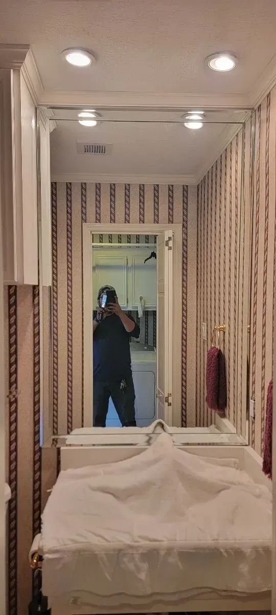 A person standing in front of a bathroom mirror, capturing a reflection of the room with striped wallpaper and a sink.
