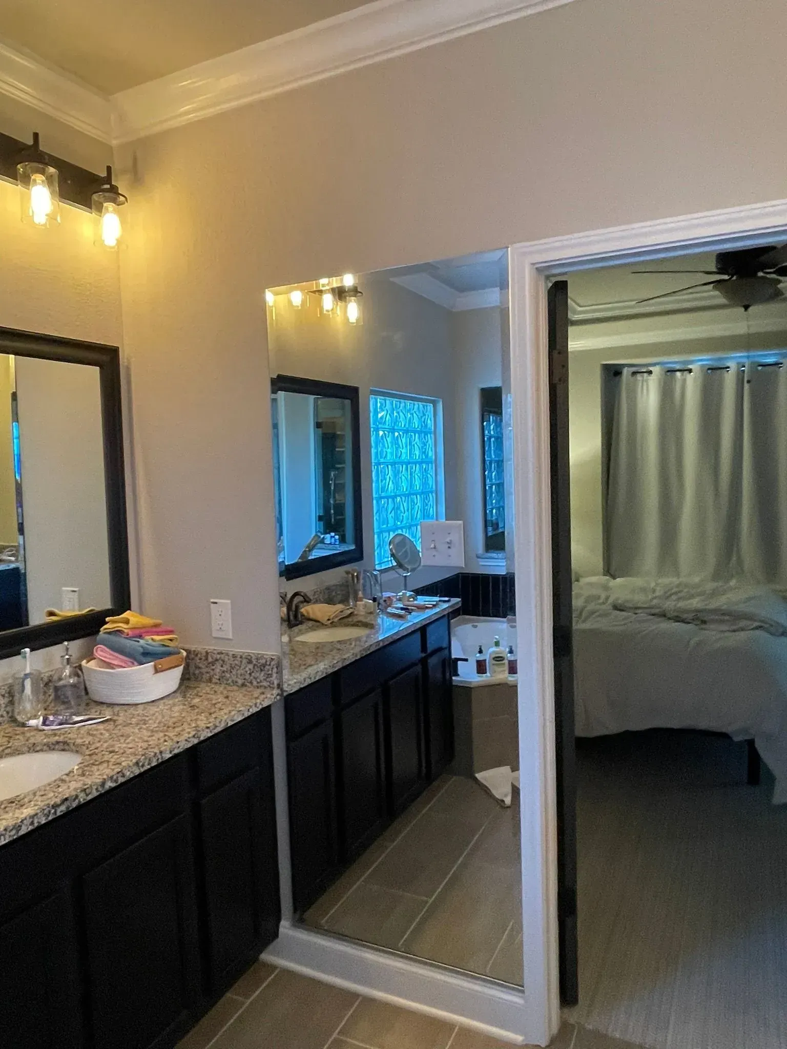 A bathroom vanity with dark cabinets and a granite countertop, featuring a mirror reflection of a nearby bedroom.