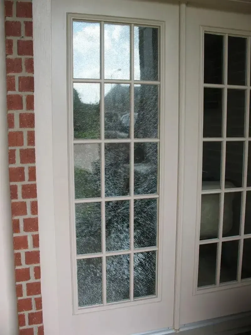 A pair of white French doors with glass panes, set beside a vertical red brick border.
