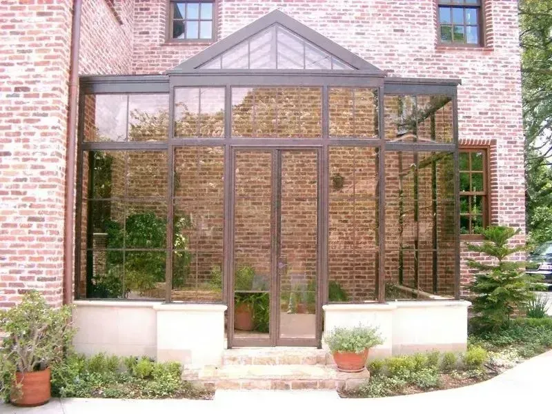 Brick house sunroom entrance with glass walls, potted plants, and a central door