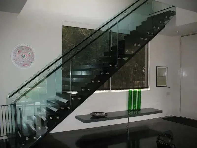 Modern interior with glass staircase, black steps, and a table with green vases.