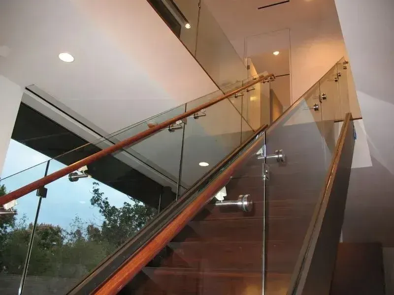 Modern staircase with glass railings and wooden handrails inside a bright building
