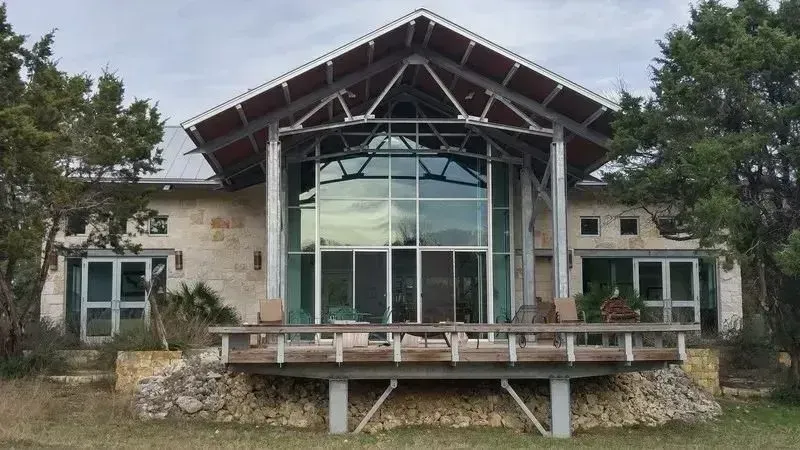 Modern stone house with a large glass entry and wooden roof, viewed from the front outdoors