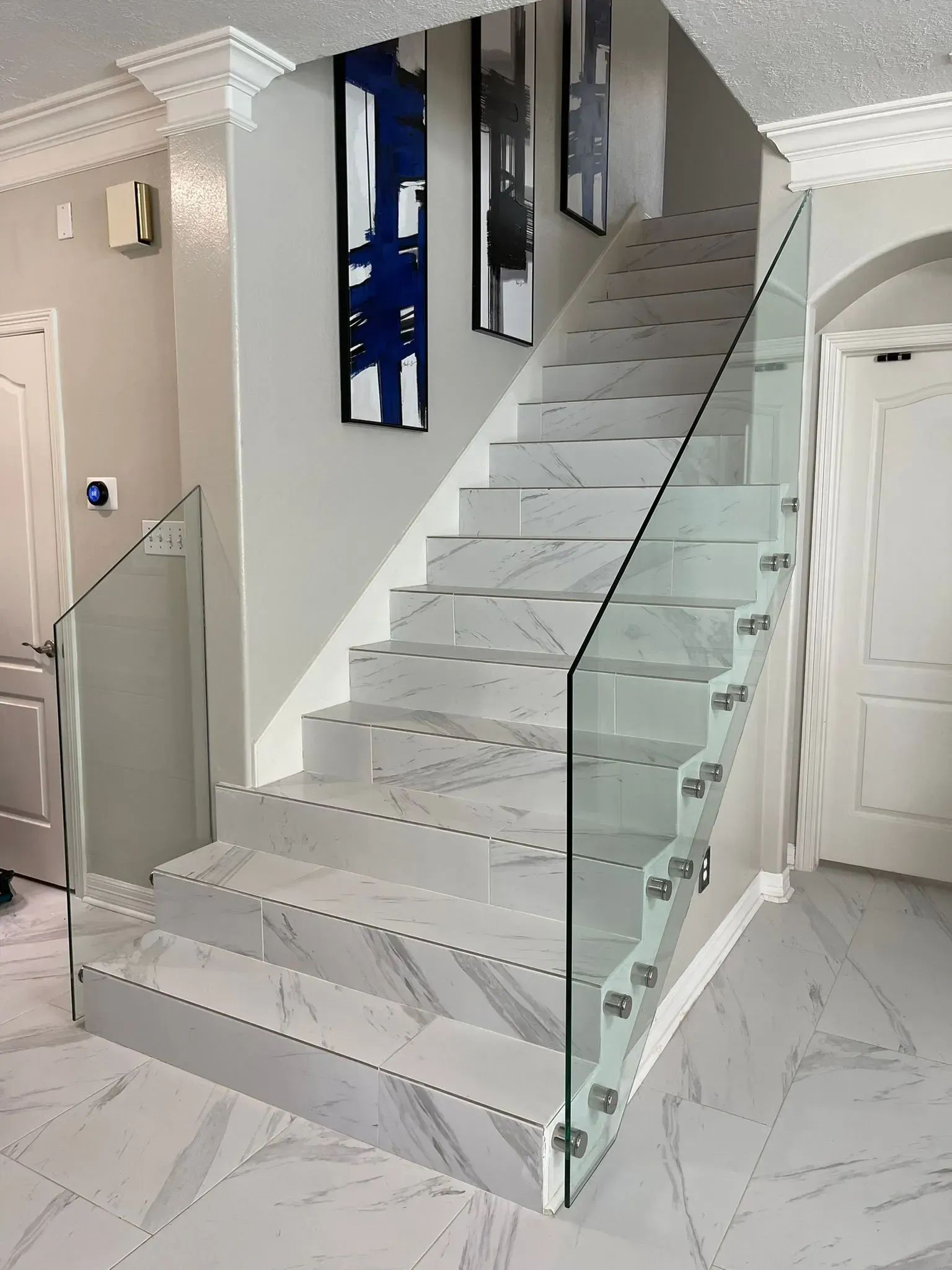 Modern indoor staircase with glass railing and gray marble steps in a white hallway