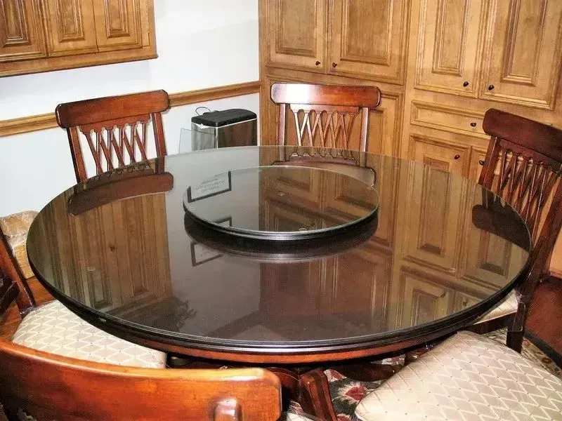 A round wooden dining table with a black glass top and matching rotating center piece, surrounded by wooden chairs.