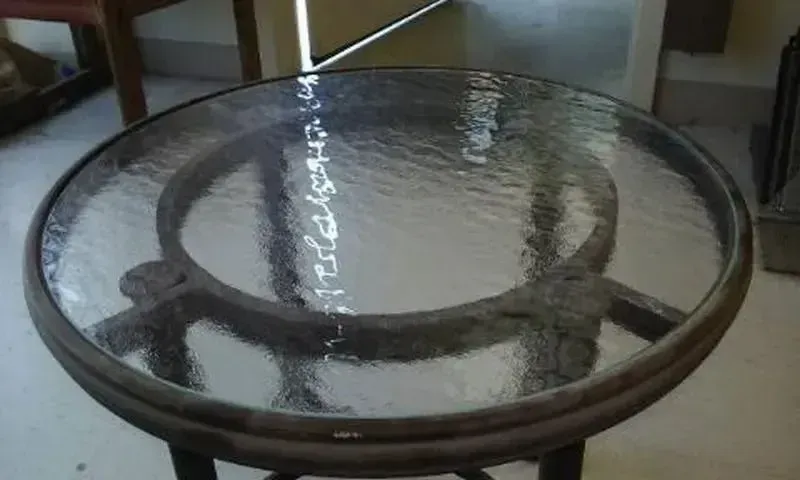 A round metal table with a textured glass top, viewed from above, situated in an indoor setting.