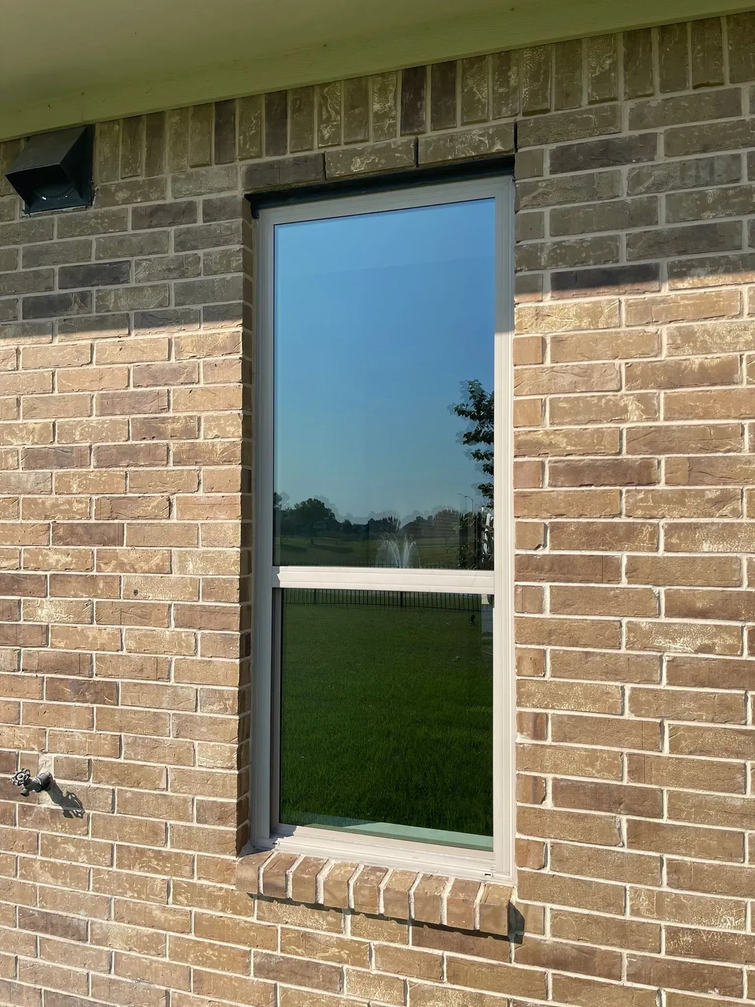 A vertical window with a reflective pane set into a light brown brick exterior wall.