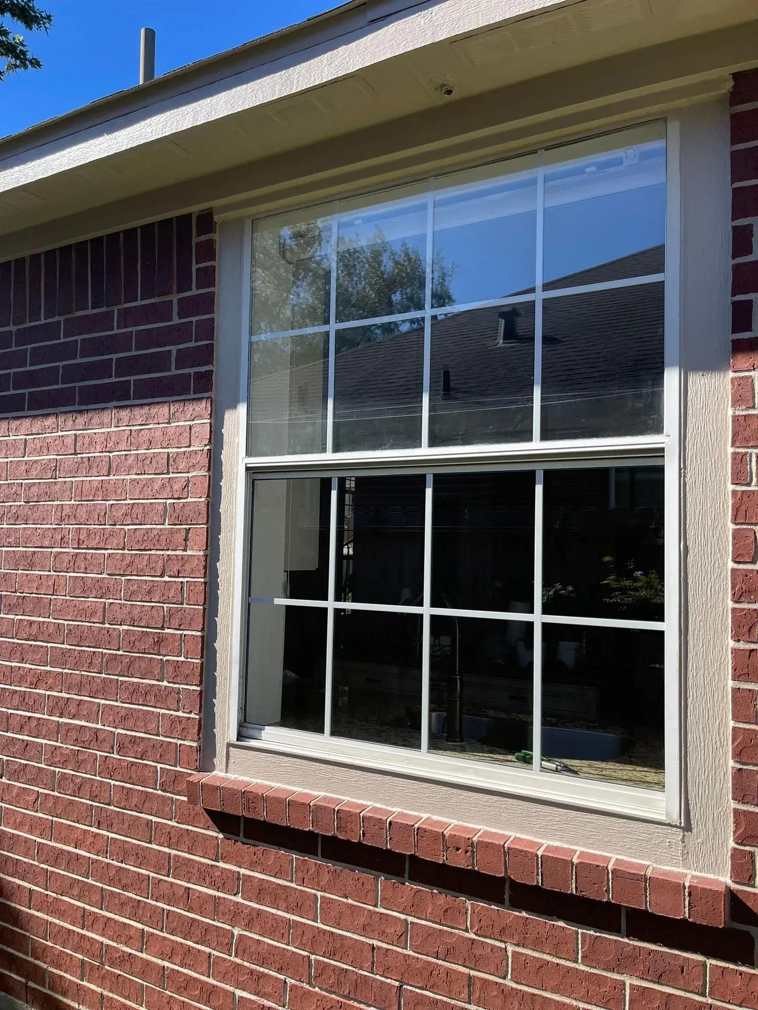 A white-framed window with a grid pattern, set into a red brick exterior wall on a sunny day.