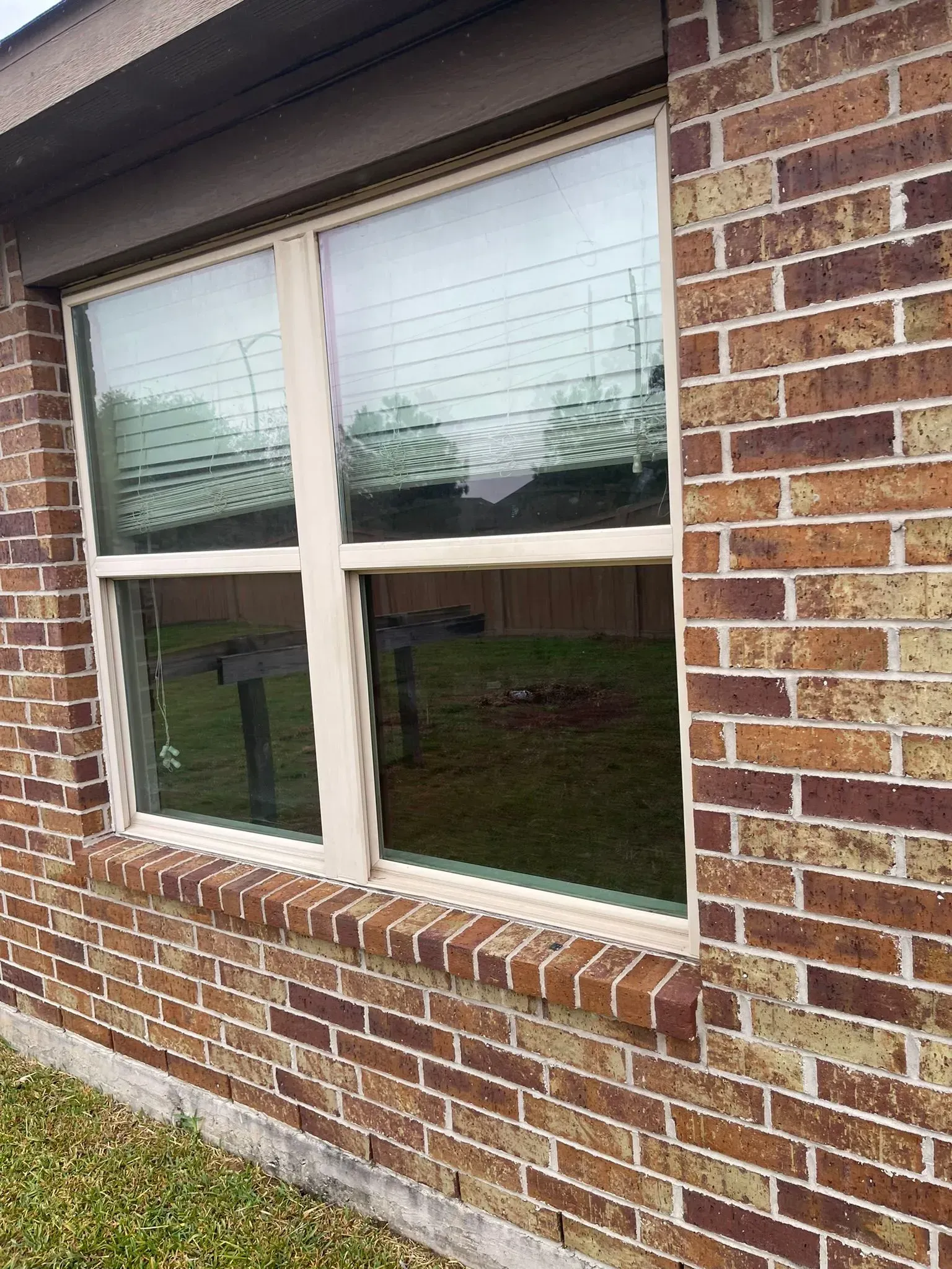 A white-framed window set into a brown brick exterior wall, showing a reflection of the outdoors.
