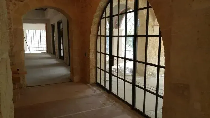 A stone hallway with an arched doorway featuring a large, black-framed metal grid door leading to an outdoor space.