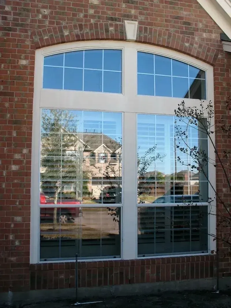 A large, arched window with a grid pattern, set within a red brick wall on a house exterior.