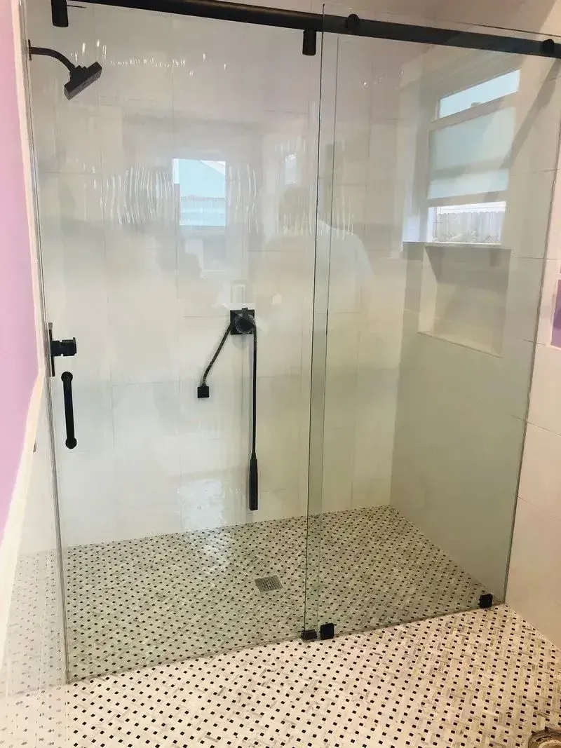 A modern walk-in shower with black hardware, a sliding glass door, and patterned tile flooring.