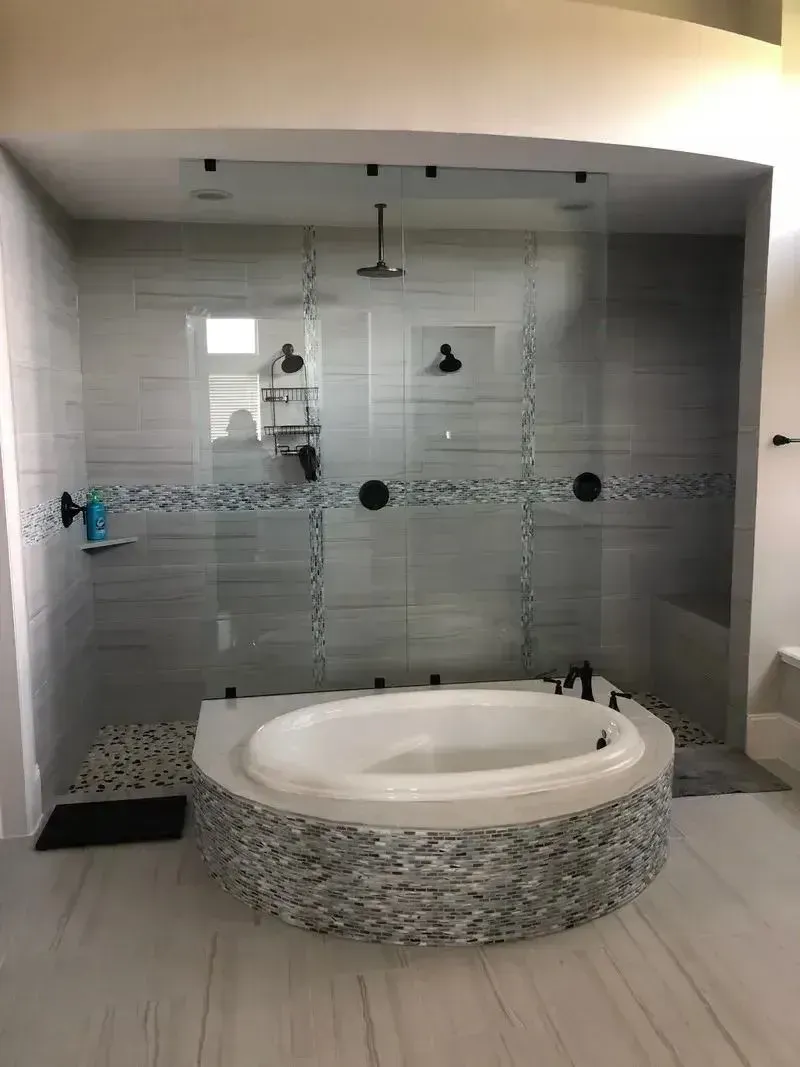 A modern bathroom features a round soaking tub with a tiled base in front of a glass-enclosed shower with grey wall tile.