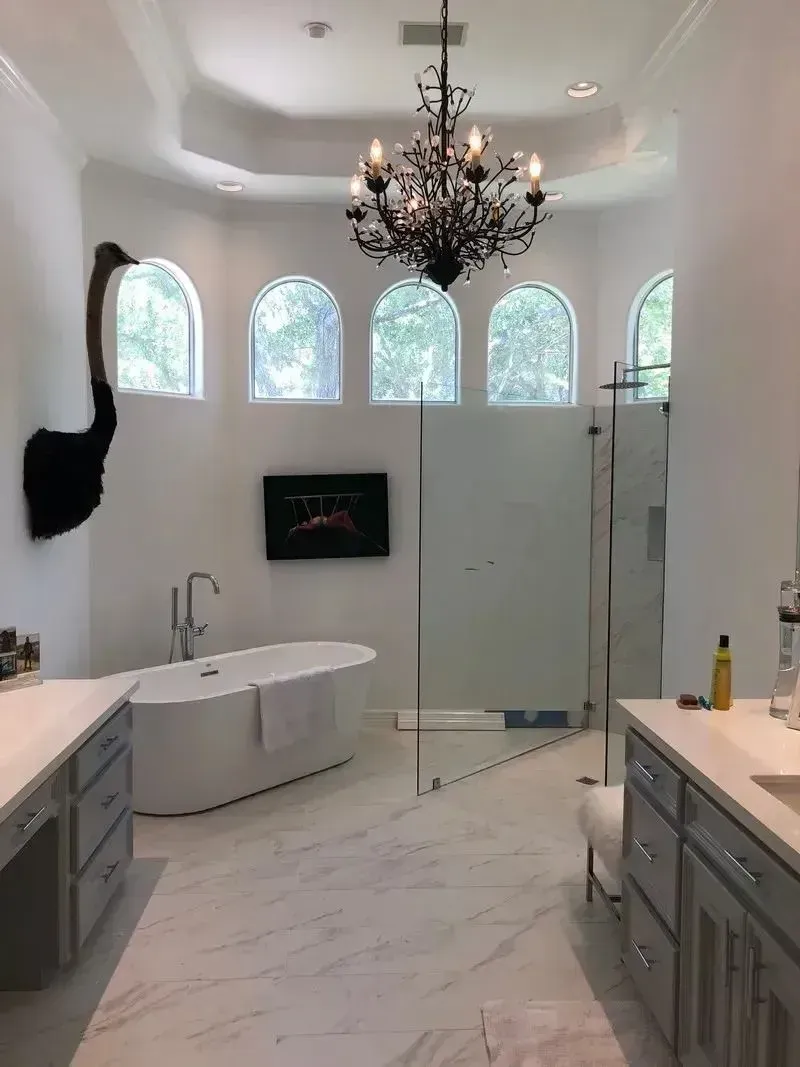 A modern, white bathroom features a freestanding tub, a walk-in glass shower, double vanities, and an ostrich wall mount.