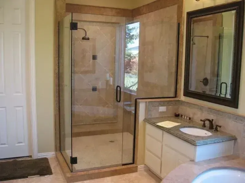 A beige-tiled bathroom featuring a glass shower stall next to a vanity with a white countertop and mirror.