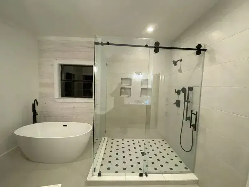 A modern bathroom featuring a white freestanding tub, a glass-enclosed shower with black hardware, and a small window.